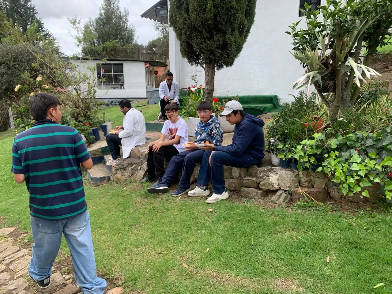 Adultos acompañantes sentados en las bancas de la zona verde del colegio